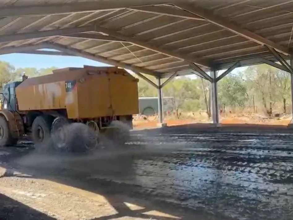 A water cart spraying binder and water across the scarified base